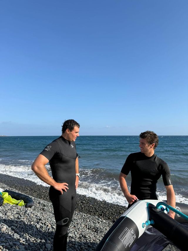 Dos riders en neopreno charlando en una playa de callaos antes de entrar al agua