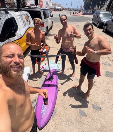El grupo celebrando en la llegada con una tabla de downwind morada y cervezas en la mano