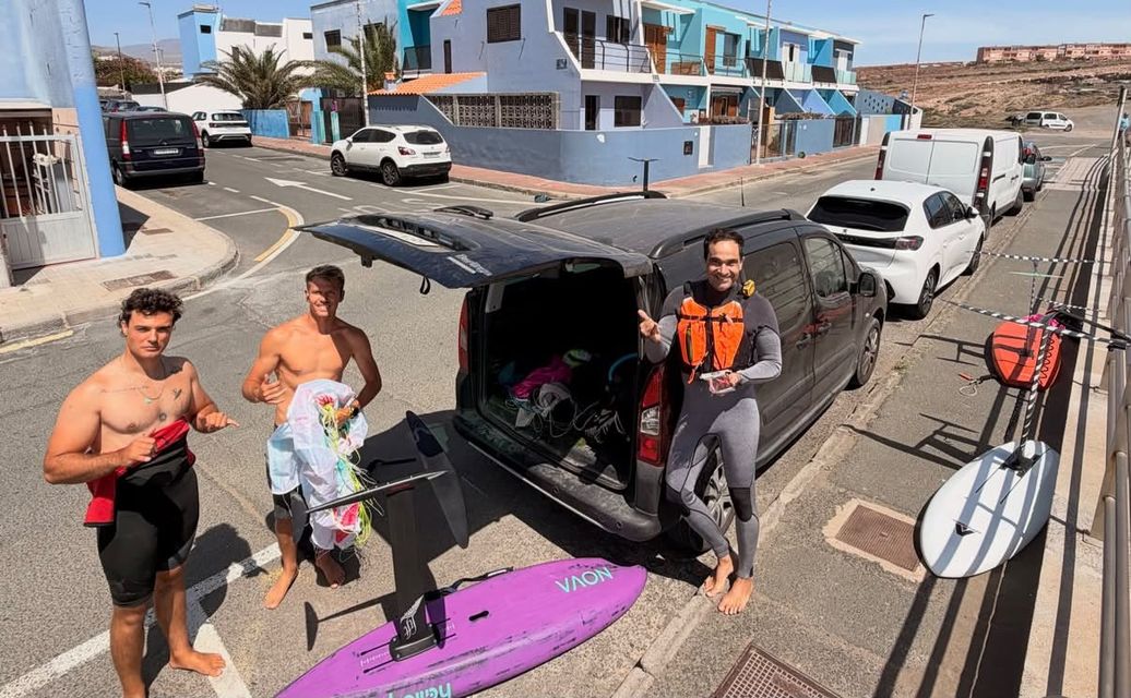 Tres riders sonrientes junto a una furgoneta con tablas y foils después del run