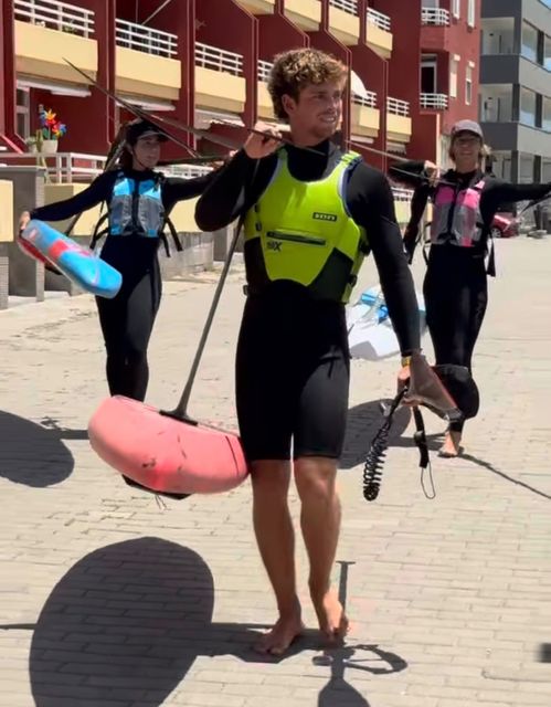 Un rider camina hacia el agua con el foil al hombro, seguido de dos riders más