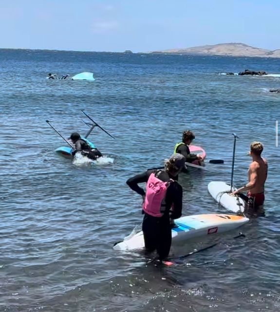 Varios riders entrando al agua con sus tablas de foil desde la orilla
